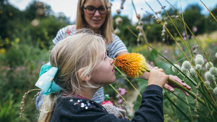 Young blonde girl smelling flower in Oxford's Botanical Garden, stood next to mother