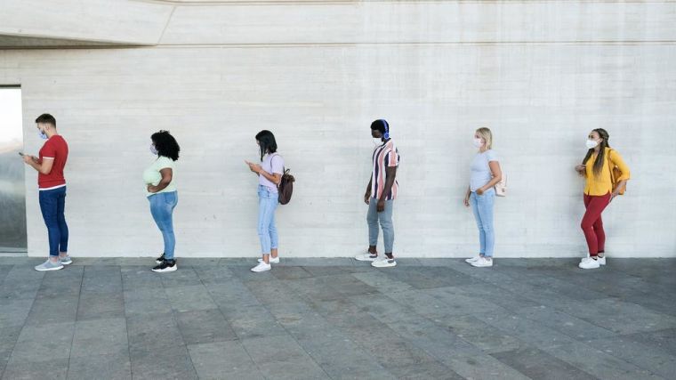 Multiracial people standing in a queue and waiting - Young people with social distancing and wearing protective face masks - Concept of the new normality and social distancing
