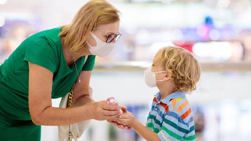 Woman bent down putting hand sanitizer into young boy's hands. Both wearing masks.