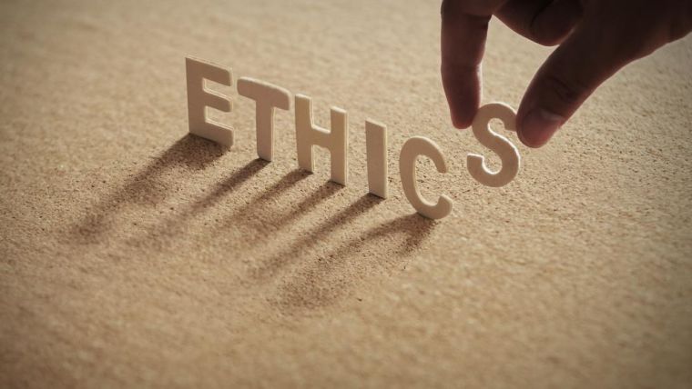 ETHICS wood word on compressed board with human's finger at S letter